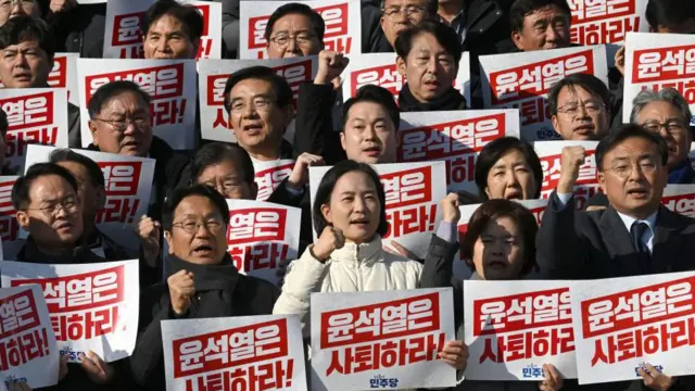 Lawmakers stand in four rows holding red ad white placards reading "Yoon Suk Yeol should resign!" during a rally against President Yoon Suk Yeol at the National Assembly in Seoul on December 4, 2024, after martial law was lifted in South Korea.